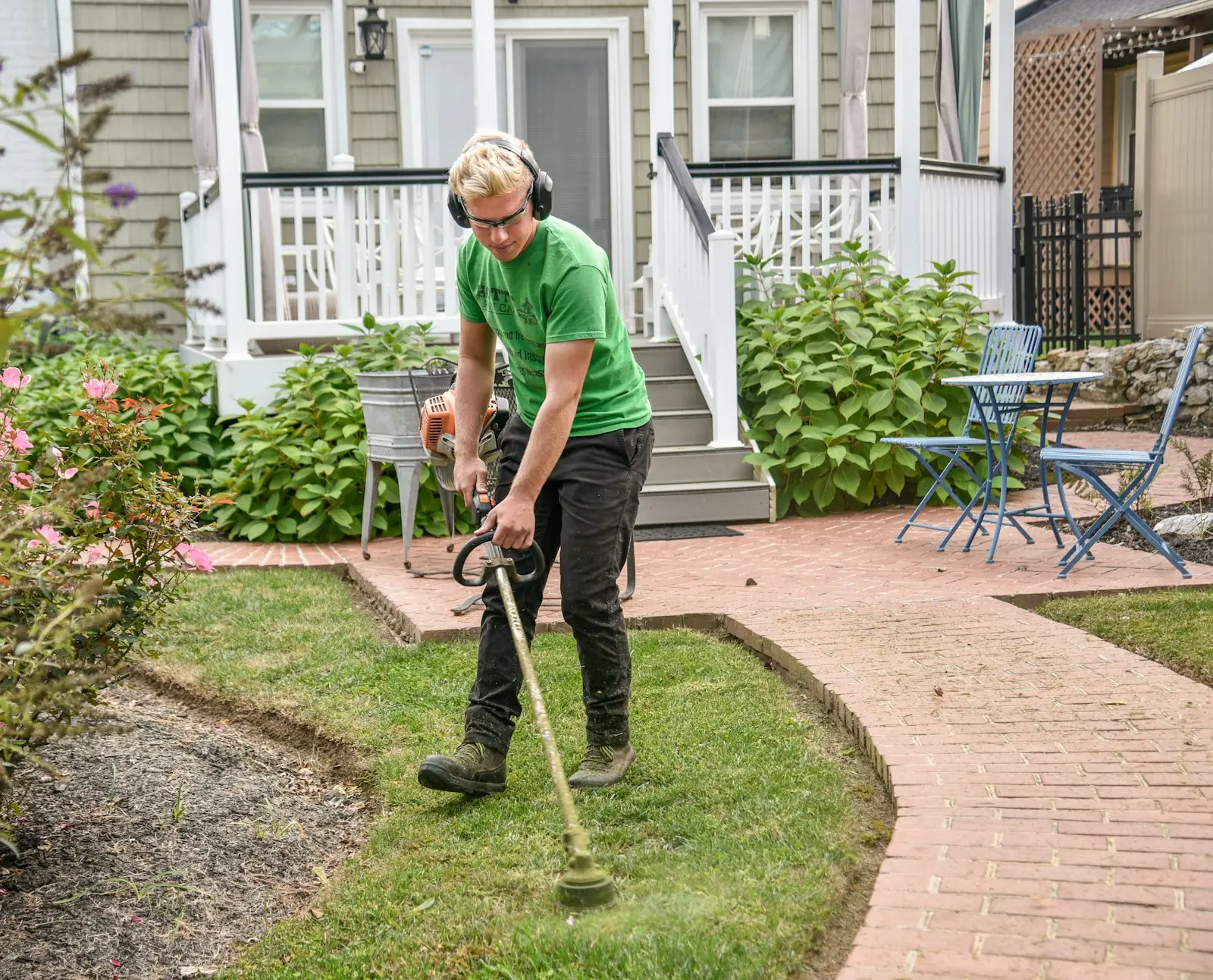 Landscaper in ear protection trimming lawn edges beside a brick path