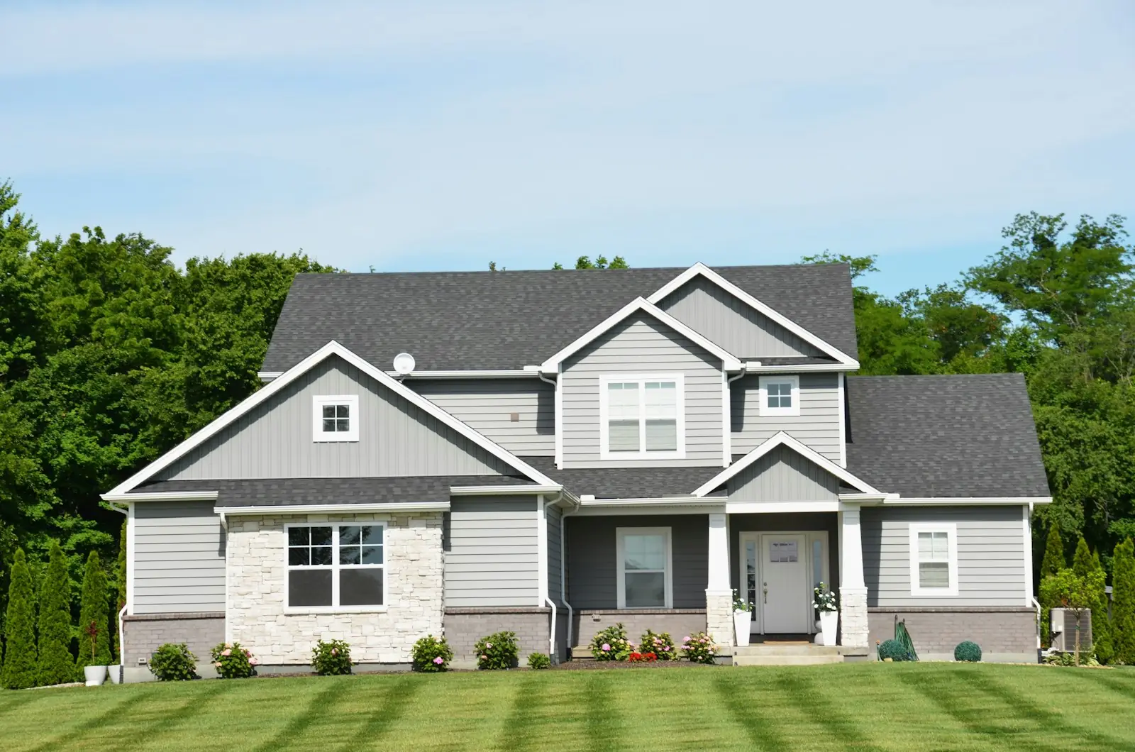 Grey two story house behind a freshly mowed, striped front lawn