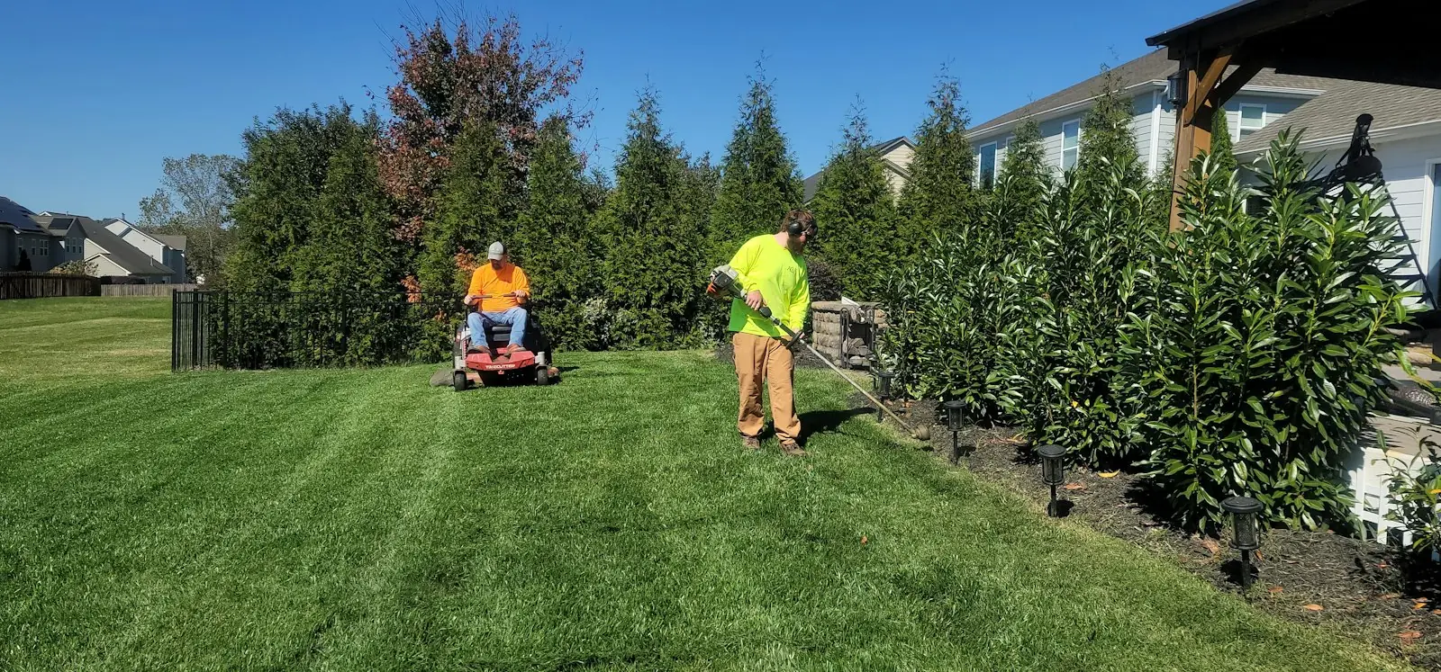 Lawn crew mowing and trimming edges in a striped backyard